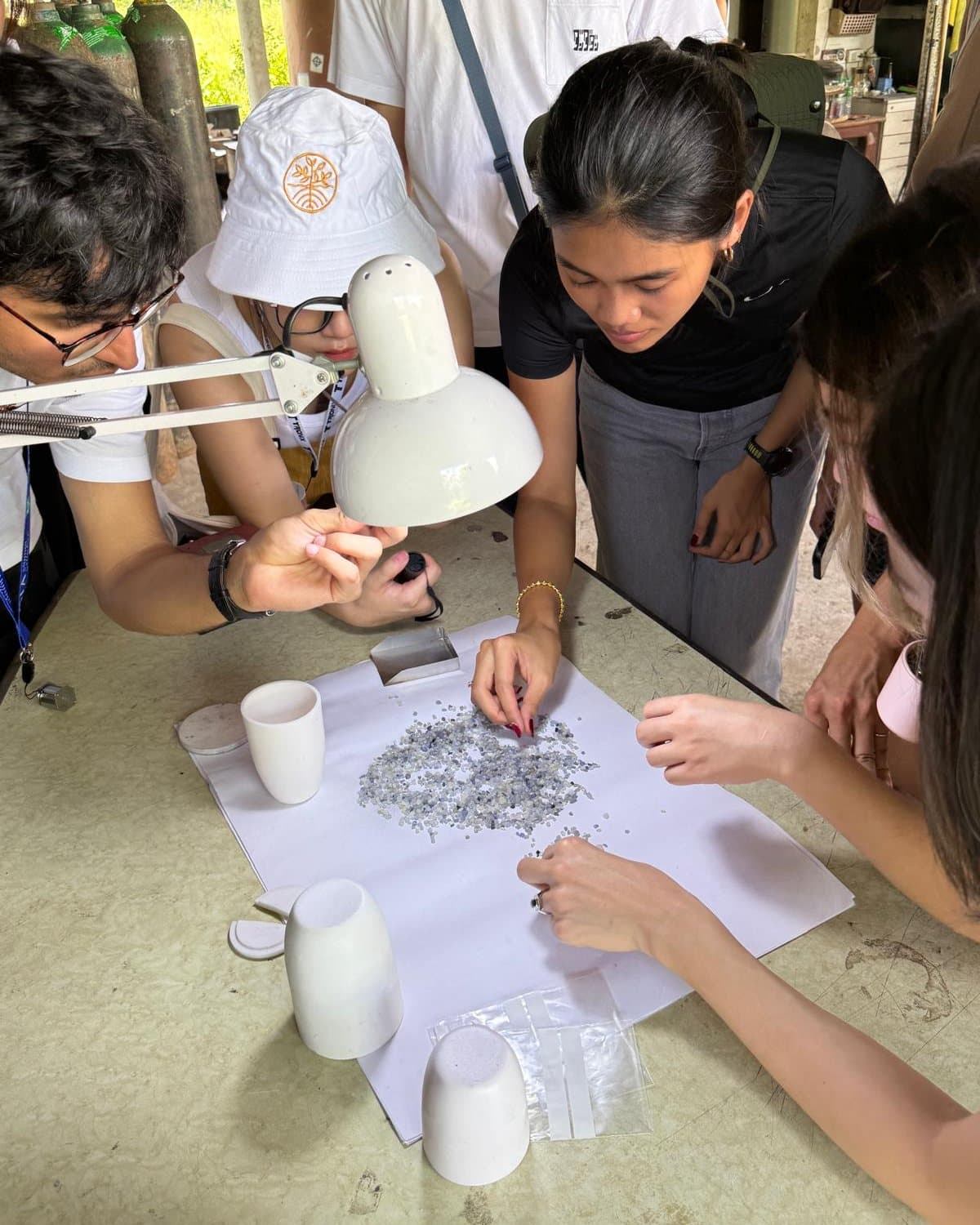 Several people leaning over a workbench under a lamp, going through a parcel of rough spread on white sorting paper